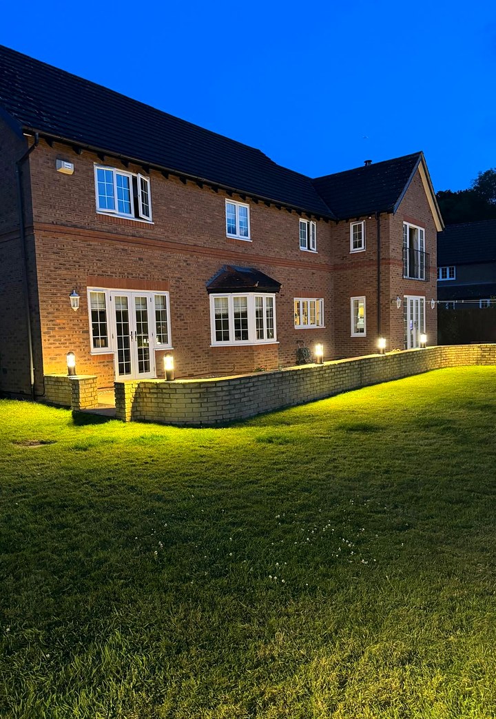 Rear of a brick house at dusk with bollard lights along a low garden wall lighting the lawn
