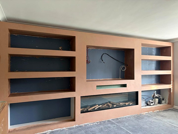 Media wall at first fix: bare plastered shelving recesses with cables ready and an electric fire fitted in the base