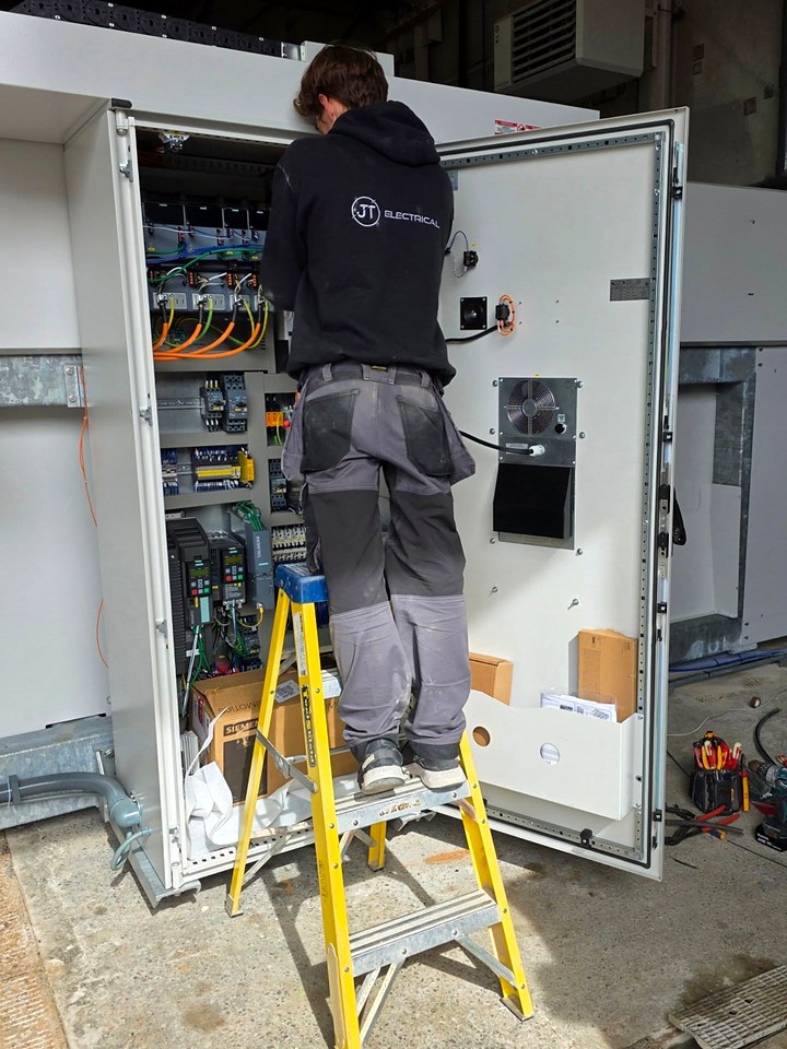 JT Electrical electrician on yellow steps wiring the control panel of an industrial machine
